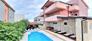 A modern apartment building with a swimming pool, outdoor seating, and a stone facade.