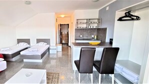 A modern hotel room with two single beds, a small kitchenette, a dining area, and a bathroom visible through an open door. - Tiffany Novalja (Novalja)