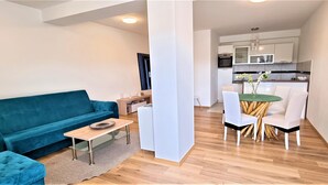 A modern living room with a blue sofa, a small wooden table, and a dining area with white chairs and a green table. - Tiffany Novalja (Novalja)