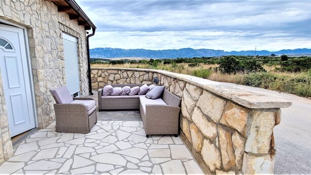 A stone building with a closed white door, a stone wall, and a patio with wicker furniture and cushions. - Tiffany Novalja (Novalja)