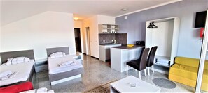 A hotel room with two beds, a small kitchenette, a dining area with a table and chairs, and a sofa.