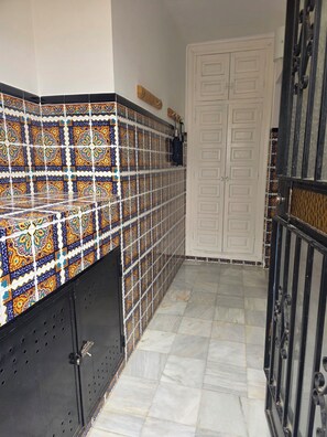 A narrow hallway with patterned tile walls, a white door, and a metal gate.