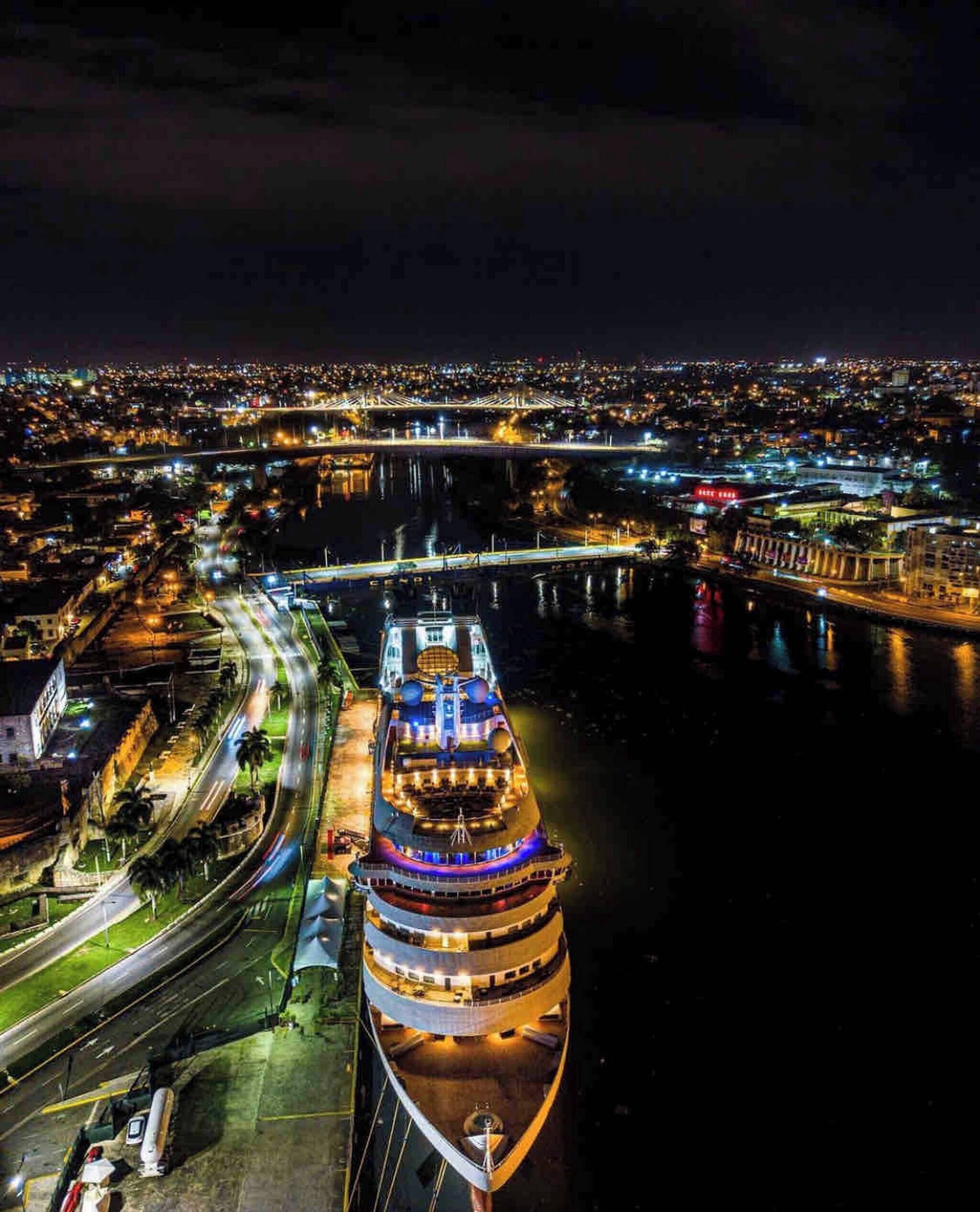 Een groot cruiseschip ligt aangemeerd in een haven, met een stadsbeeld op de achtergrond.