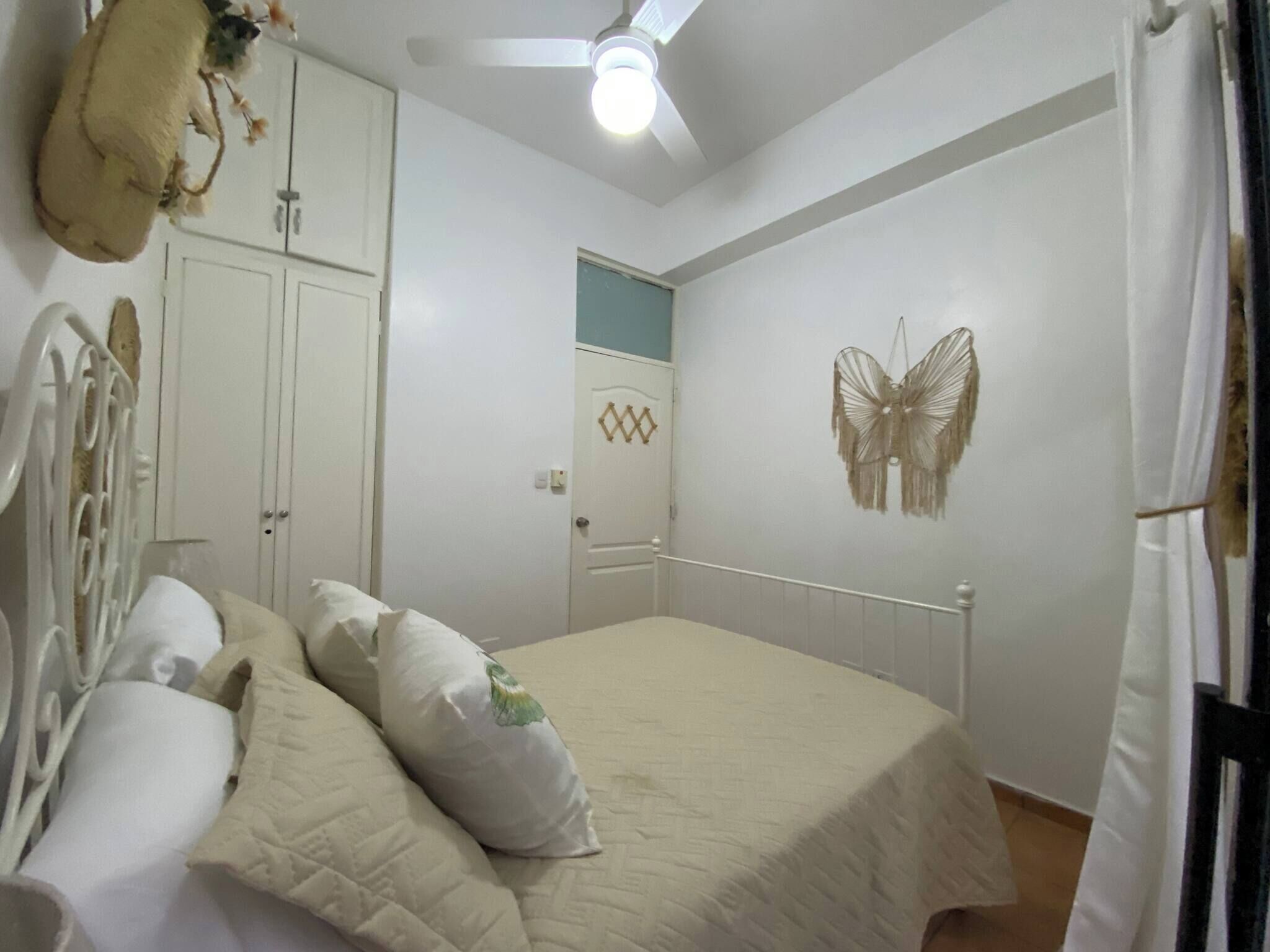 A bedroom with a bed, pillows, a ceiling fan, a wall-mounted butterfly decoration, and a wardrobe.