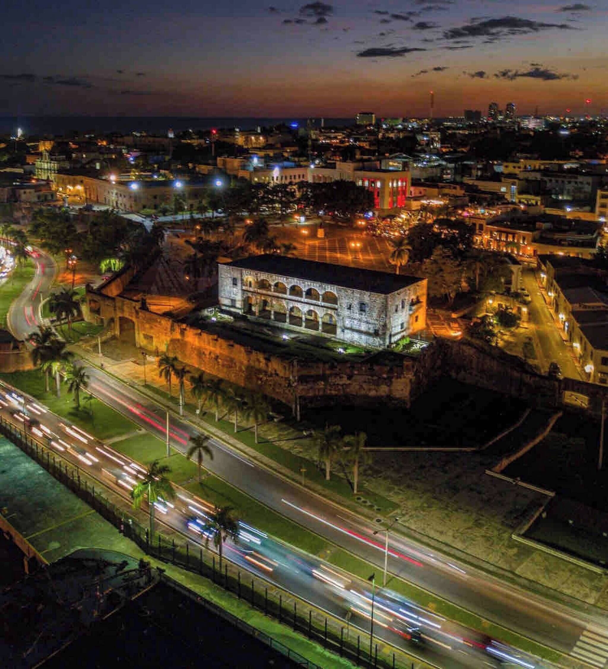 A historic building with arched windows and a central courtyard, surrounded by modern roads and city lights.