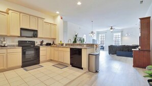 A modern kitchen with a dishwasher, oven, and microwave. There is a dining area with a sofa and a small table. - Beautifully Furnished Condo in Villages of Five Points (Lewes)