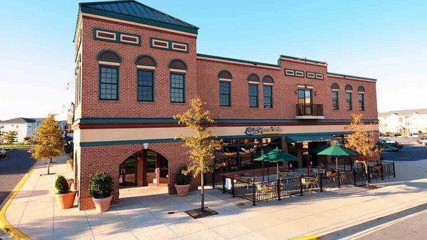 A brick building with a green awning and outdoor seating area. - Beautifully Furnished Condo in Villages of Five Points (Lewes)