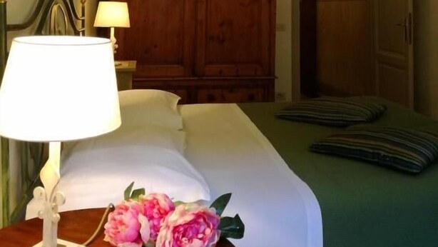 A hotel room with a bed, a wooden wardrobe, a chandelier, and a nightstand with a lamp and flowers. - Dimora Pieri - Corsini Apartment, historic building  in the old center with lift and terrace (Firenze)