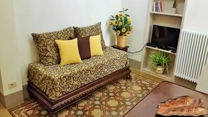 A living room with a patterned sofa, a small table, a TV, and a radiator. - Dimora Pieri - Corsini Apartment, historic building  in the old center with lift and terrace (Firenze)
