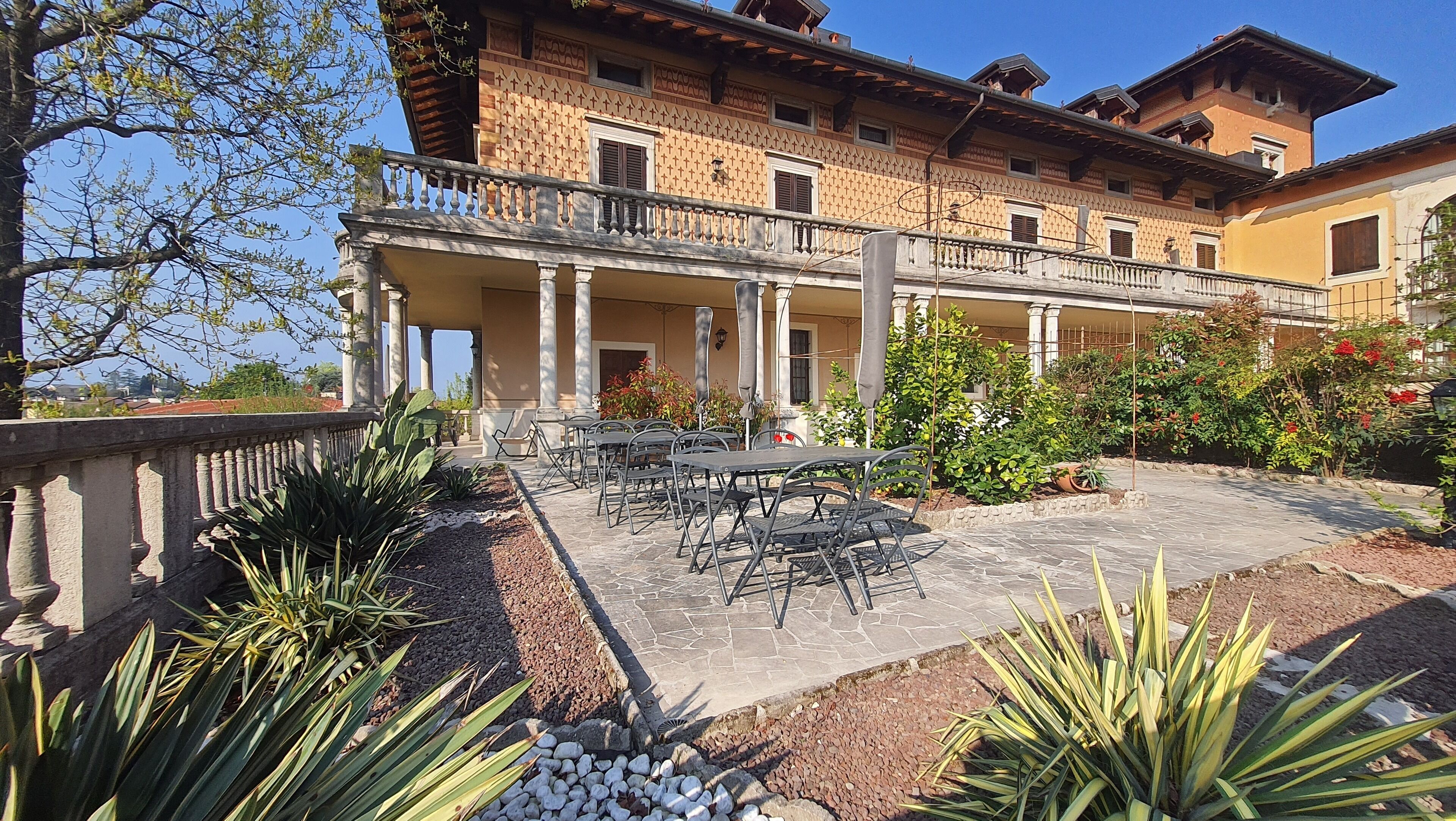 Ein Gebäude mit überdachter Terrasse, Sitzgelegenheiten im Freien und einem Garten.