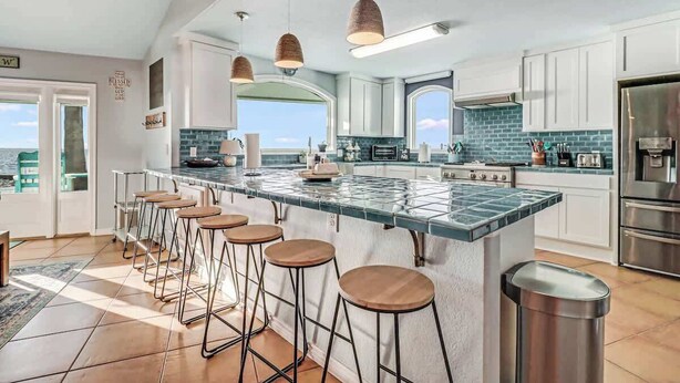 Uma cozinha moderna com uma grande ilha, banquetas, eletrodomésticos de aço inoxidável e vista para o exterior.