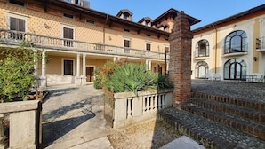 A courtyard with a stone floor, a brick wall with a gate, and a building with a balcony and windows. - Villa Santa Caterina - Three-room apartment with garden and swimming pool view (Manerba del Garda)