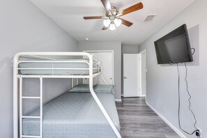 Een kamer met stapelbedden, een plafondventilator, een aan de muur bevestigde televisie en een deur naar een andere kamer.