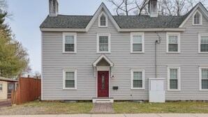 Una casa de dos pisos con puerta principal roja, detalles blancos y una chimenea.