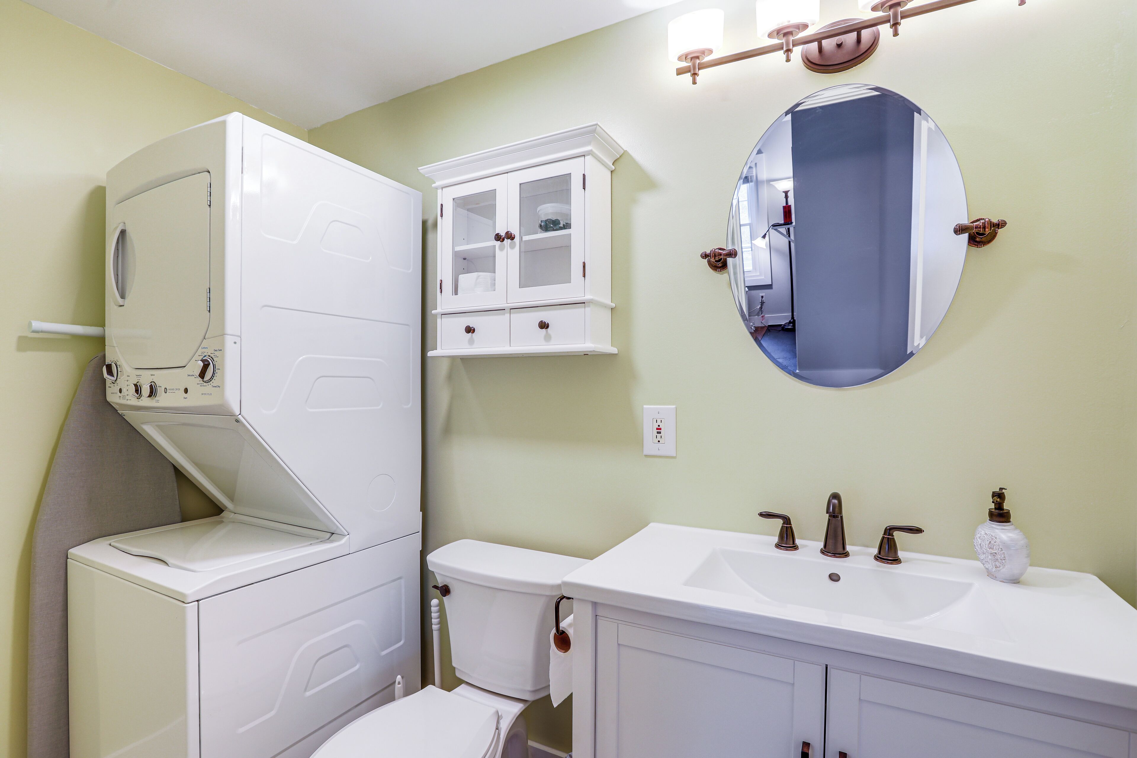 A bathroom with a built-in washer and dryer, a white vanity with a sink, and a round mirror.