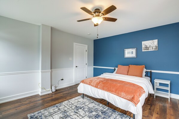 A bedroom with a bed, a ceiling fan, a white door, and a blue wall. - In-town & Walkable: Historic Yardley Retreat! (Morrisville)