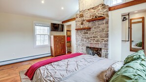Un dormitorio con chimenea de piedra, vigas de madera, una cama grande y un armario.