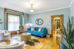 Una sala de estar con un sofá azul, un sillón blanco, una mesita de centro de mimbre y un espejo grande.