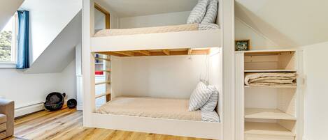 A bunk bed room with a skylight, wooden flooring, and a built-in storage unit.