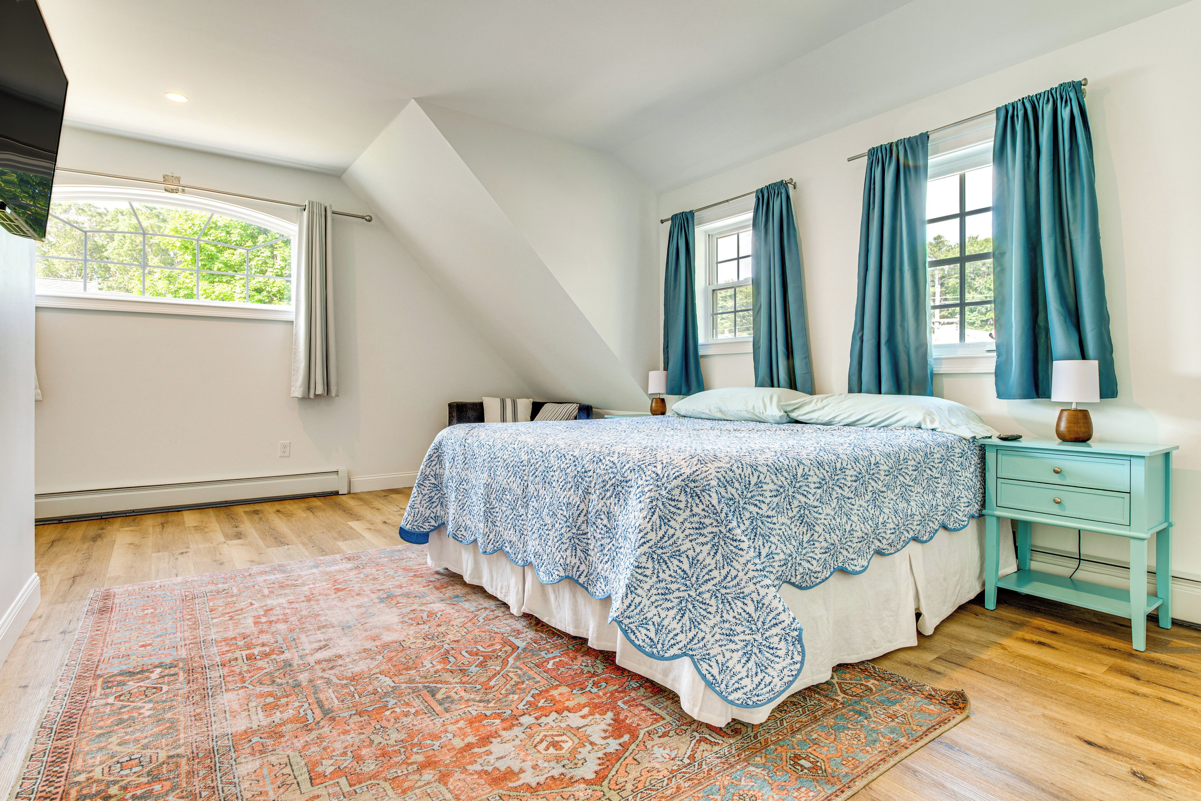 A bedroom with a large bed, a nightstand, a window with curtains, and a patterned rug.