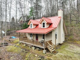 Una cabaña de dos pisos con techo rojo, una terraza de madera y una chimenea.