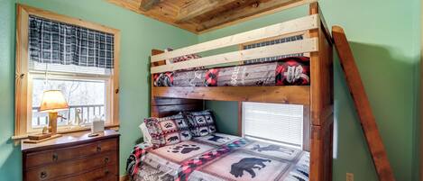 A bunk bed with a plaid bedspread, a dresser with drawers, a window with blinds, and a wooden ceiling.