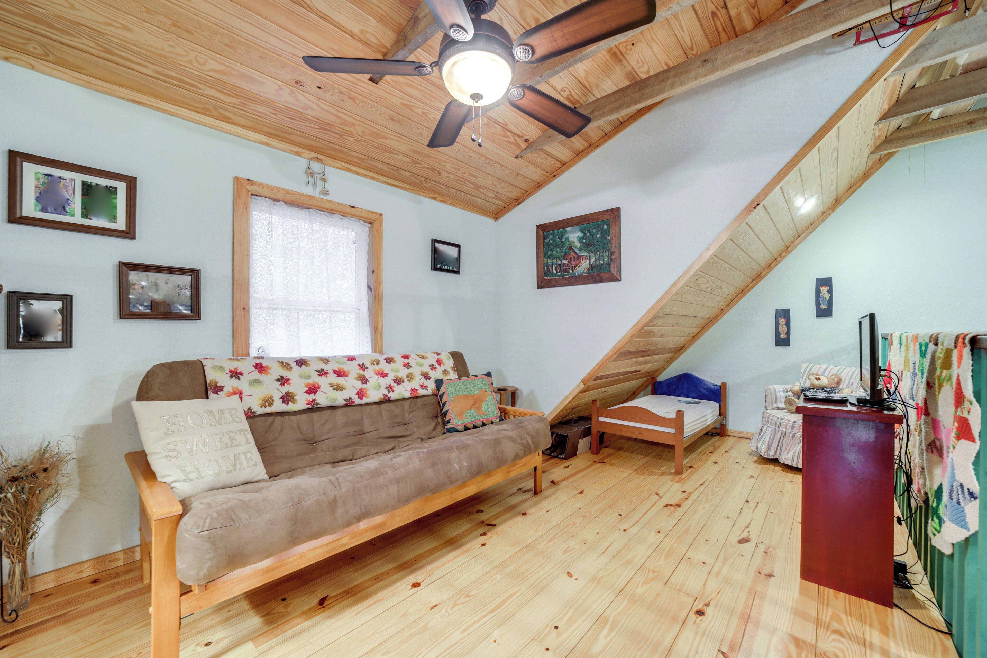 A cozy loft bedroom with a wooden ceiling, a sofa bed, a small desk, and a window with curtains.