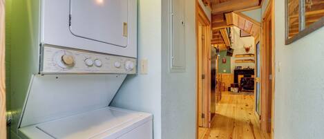 A laundry area with a washing machine and dryer, wooden flooring, and a hallway leading to a kitchen area.