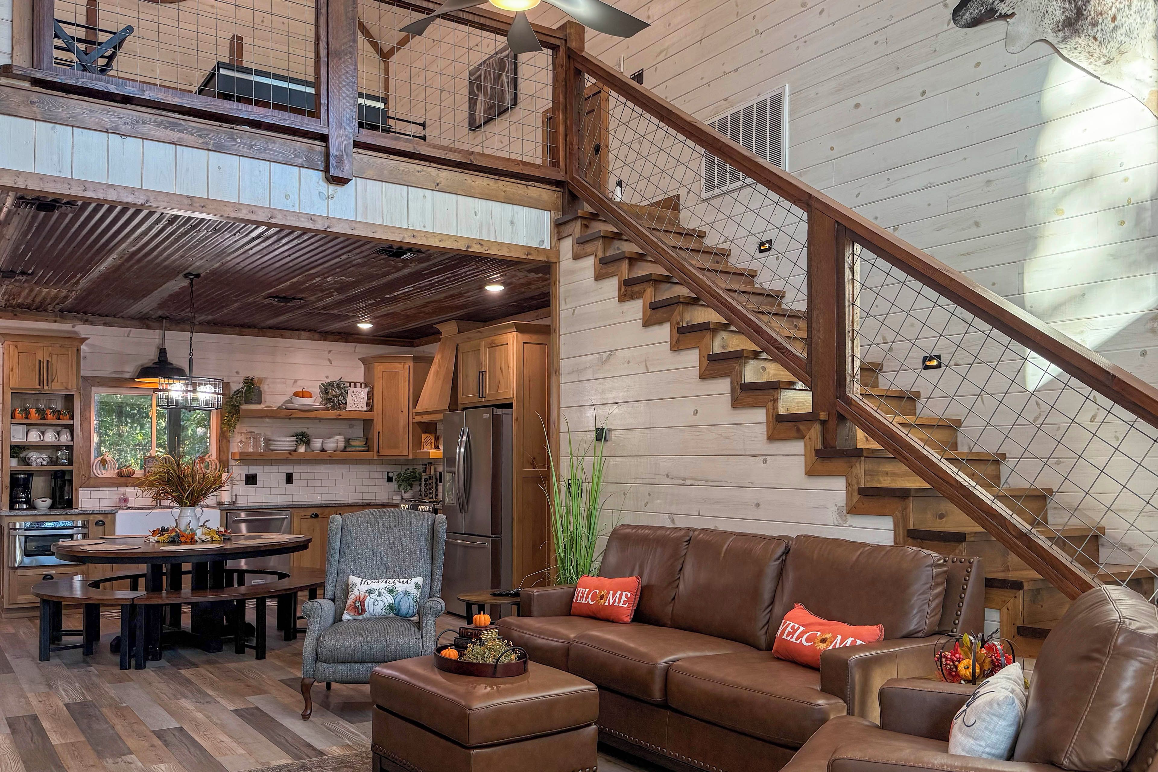 A spacious living area with a wooden staircase, a dining table, and a kitchen in the background.
