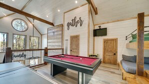 Une table de billard dans une pièce aux murs en bois et dont le plafond est orné de poutres apparentes.