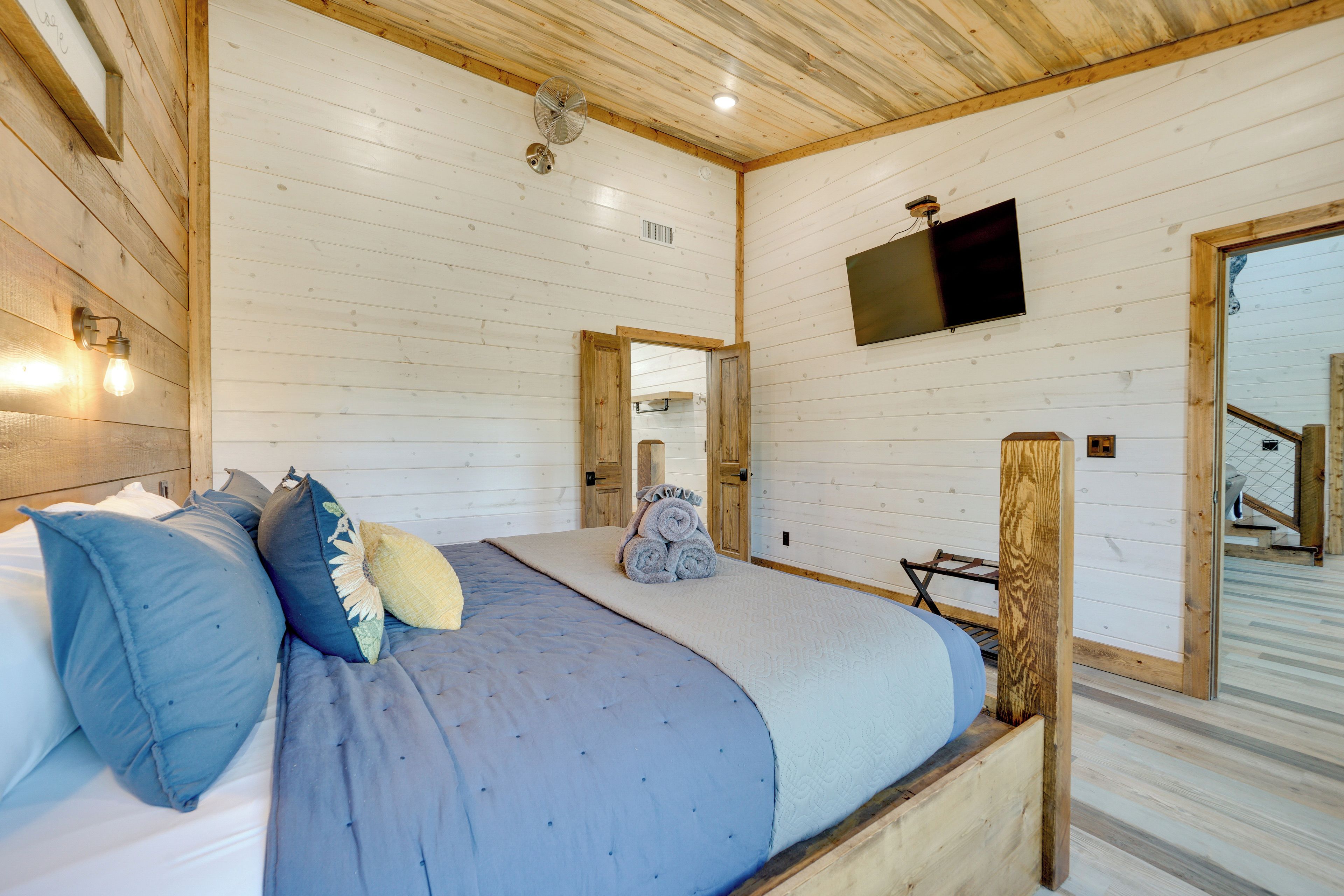 Ein Schlafzimmer mit einem Bett, Kissen, einem Ventilator und einem an der Wand montierten Fernseher.