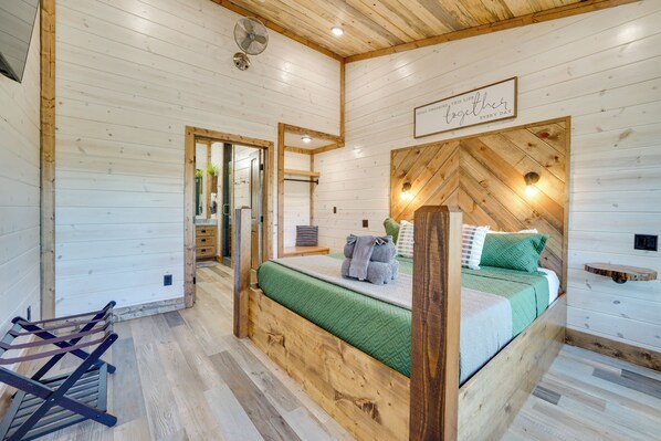 Een slaapkamer in een houten blokhut met een bed, een houten hoofdbord, een ventilator aan de muur en een bord boven het bed.