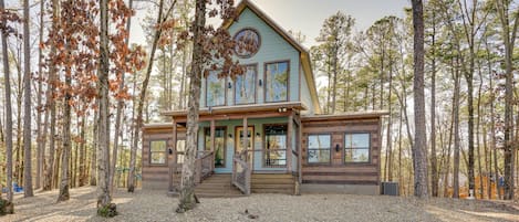 A two-story cabin with a front porch, surrounded by trees.