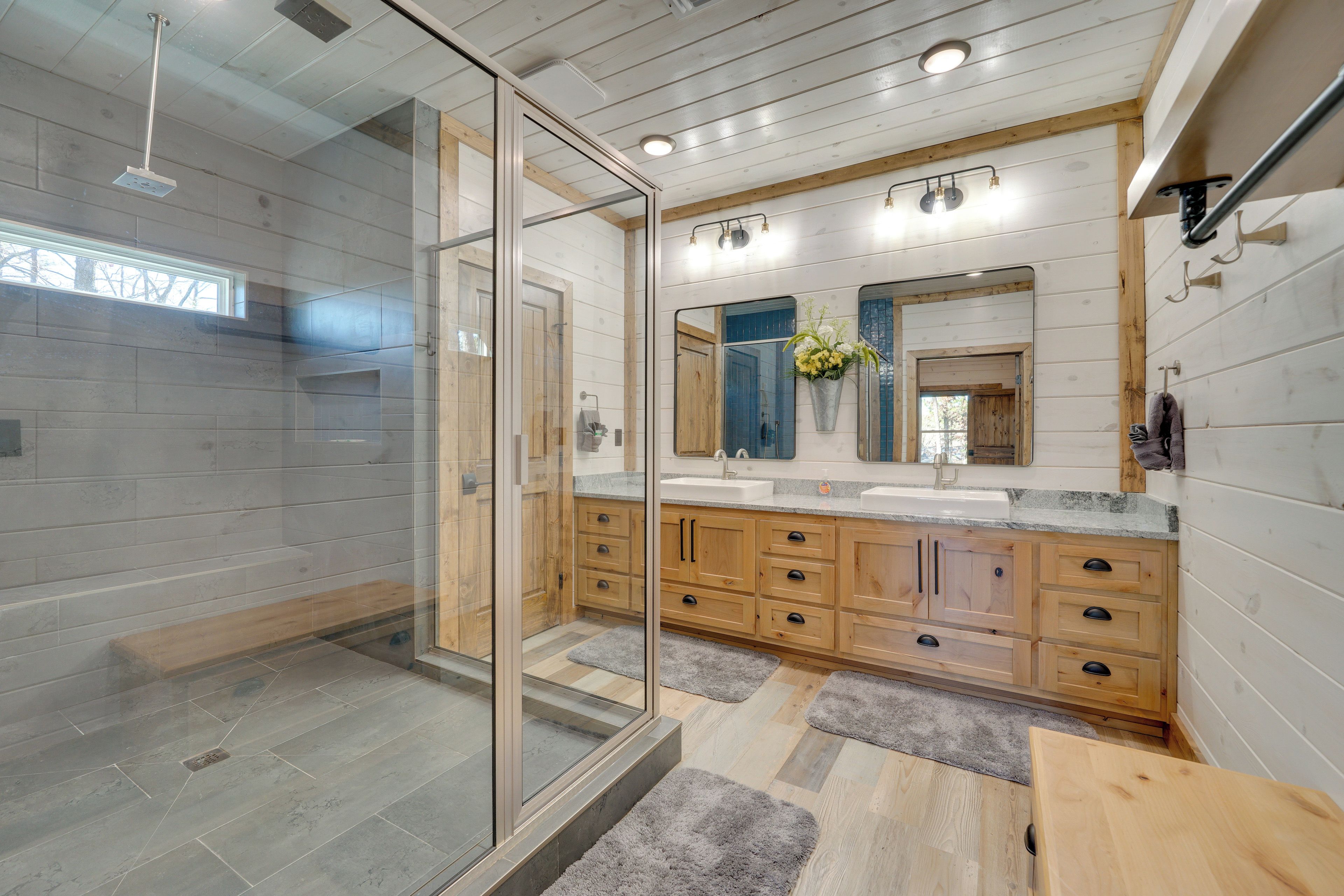 A modern bathroom with a glass-enclosed shower, wooden cabinets, a large mirror, and a granite countertop.