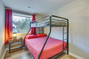 A bunk bed with a red bedspread, a bedside table with a lamp, and a window with red curtains. - Comfy Kingsport Apartment - Walk to Brewery! (Kingsport)