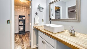 A bathroom with a wooden vanity, white sink, and a large mirror. There is a towel rack with folded towels and a shelf with more towels. - Home 2.5 Mi to Fort Stewart w/ Heated Pool (Hinesville)