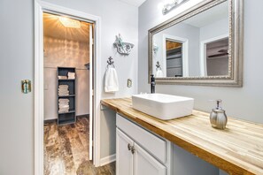 A bathroom with a wooden vanity, white sink, and a large mirror. There is a towel rack with folded towels and a shelf with more towels. - Home 2.5 Mi to Fort Stewart w/ Heated Pool (Hinesville)
