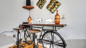 A room with a wooden floor, a black bicycle, a wooden stool, a table with decorative items, and a wall with two framed artworks. - Home 2.5 Mi to Fort Stewart w/ Heated Pool (Hinesville)