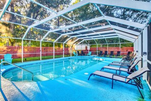 A covered outdoor swimming pool with lounge chairs and a fenced area.