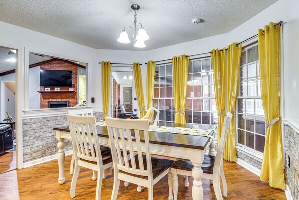 A dining area with a brick fireplace, a TV mounted on the wall, and yellow curtains on the windows. - Home 2.5 Mi to Fort Stewart w/ Heated Pool (Hinesville)