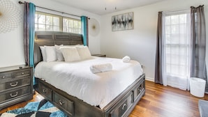 A bedroom with a large bed, a ceiling fan, a window with curtains, and a wall art piece. - Home 2.5 Mi to Fort Stewart w/ Heated Pool (Hinesville)