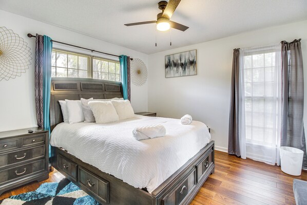 A bedroom with a large bed, a ceiling fan, a window with curtains, and a wall art piece. - Home 2.5 Mi to Fort Stewart w/ Heated Pool (Hinesville)