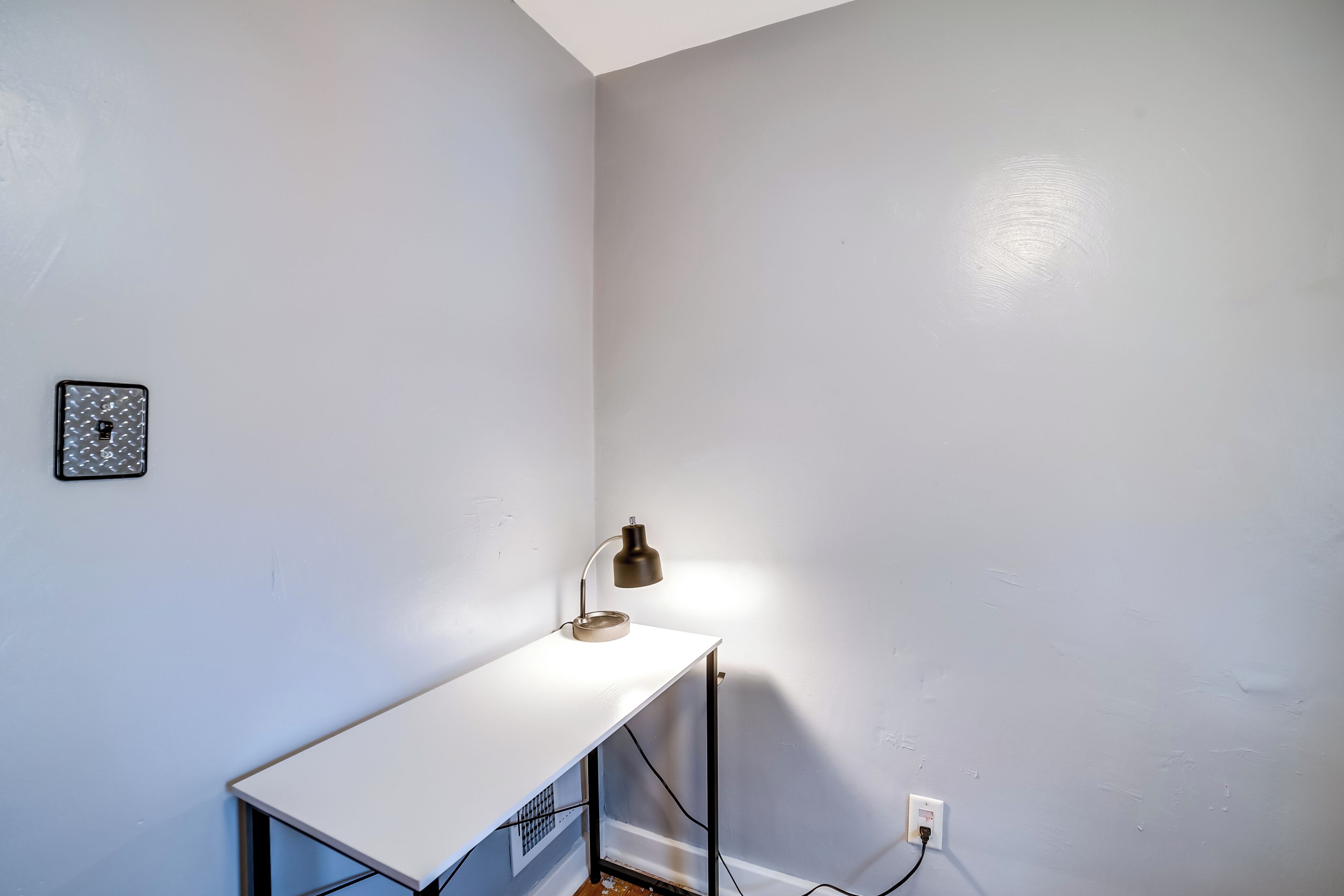 Een klein, wit bureau met een lamp, een stopcontact en een fotolijst aan de muur.