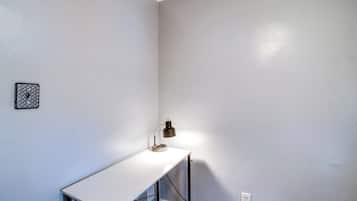 Een klein, wit bureau met een lamp, een stopcontact en een fotolijst aan de muur.