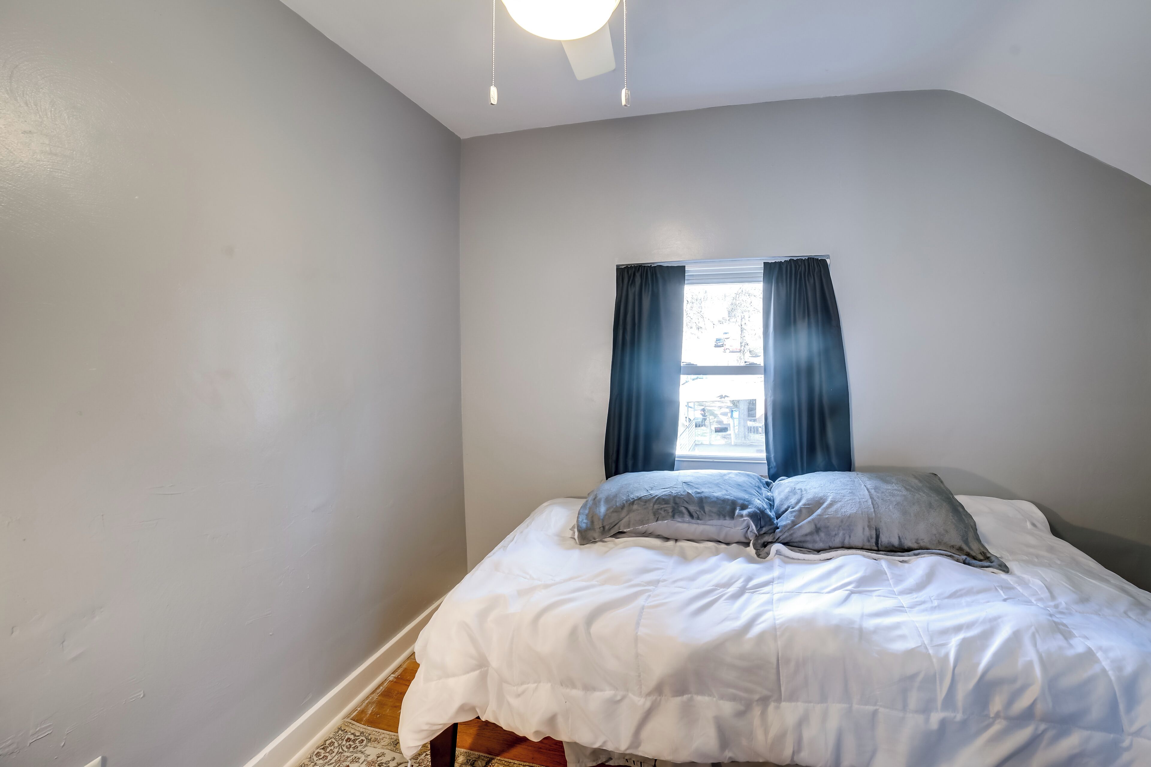A bedroom with a bed, a window with curtains, and a ceiling light.