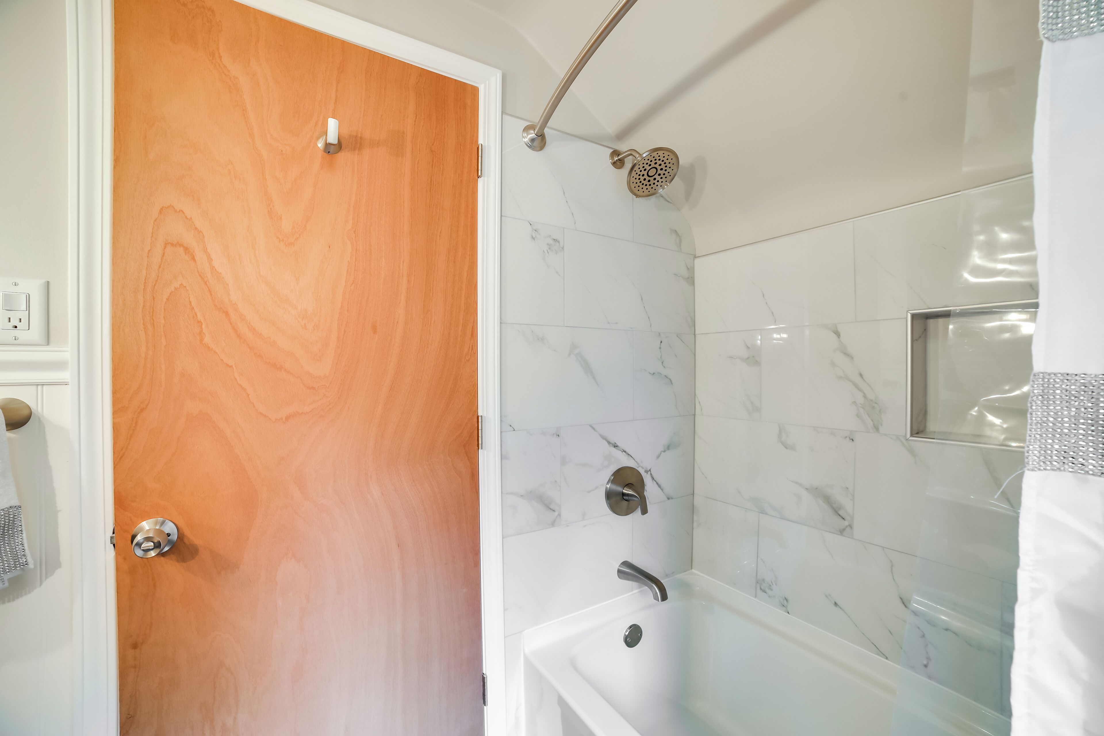 Une salle de bain avec une porte en bois, une baignoire blanche et une douche dotée d’un pommeau de douche à effet pluie.