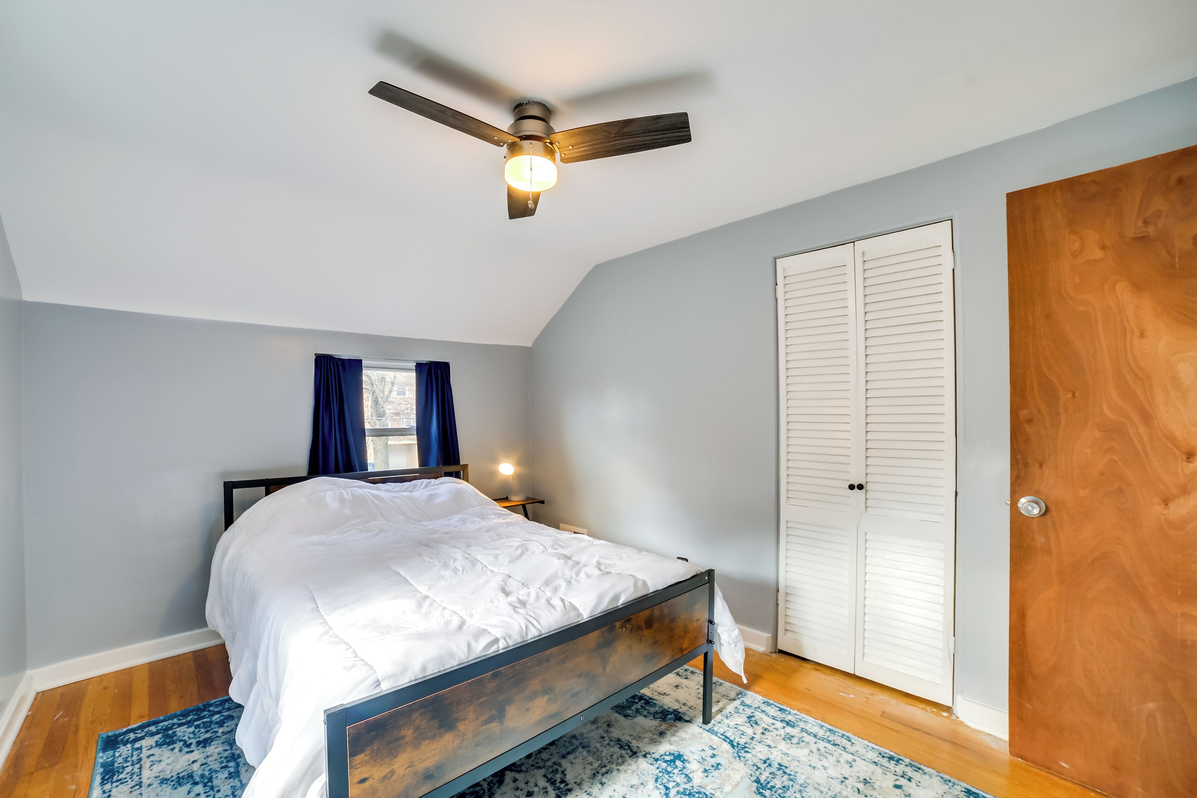 A bedroom with a bed, a ceiling fan, a wooden door, and a window with curtains.
