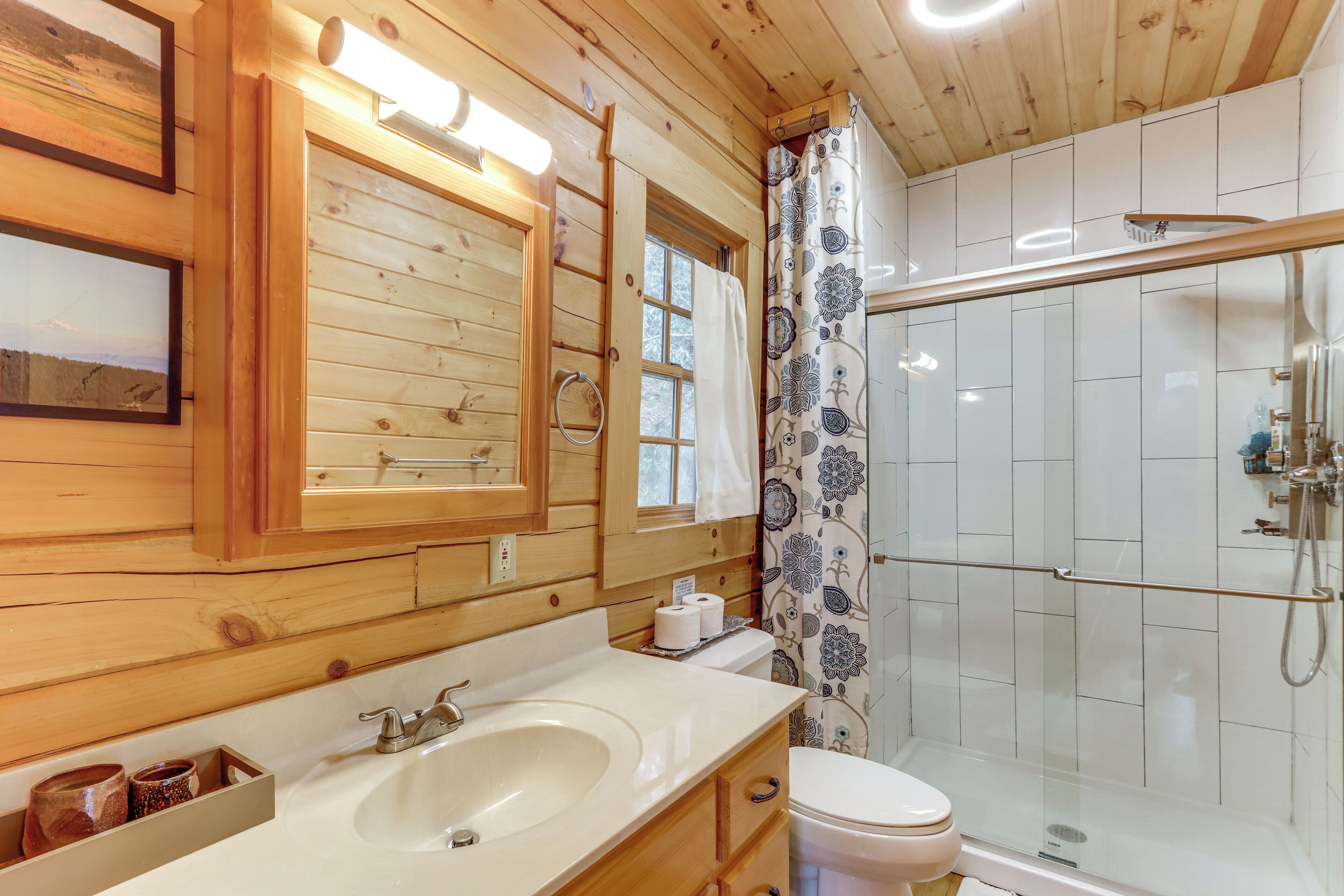 A wooden cabin bathroom with a large mirror, sink, toilet, and glass-enclosed shower.