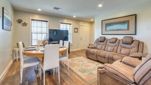 A living room with a brown leather sofa, a dining table with chairs, a TV, and a framed picture on the wall.