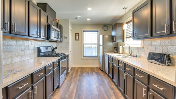 A modern kitchen with dark cabinets, a stainless steel refrigerator, a microwave, and a toaster.